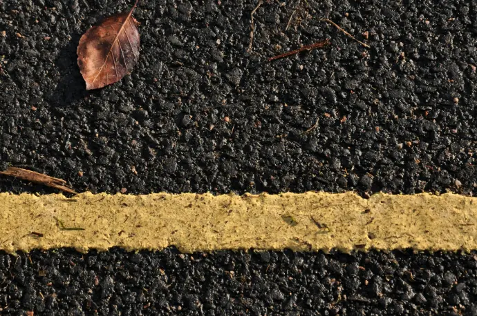 a yellow line painted on a road with a leaf on it
